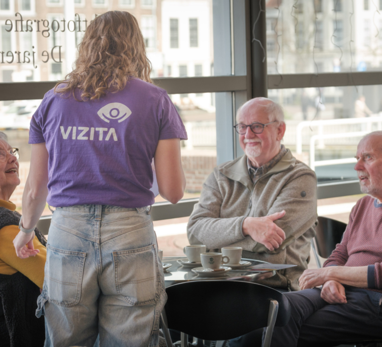 Een jongere praat met ouderen in een café.
