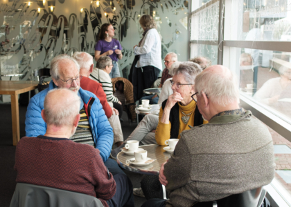 Een groep ouderen zit samen in een café en praat.