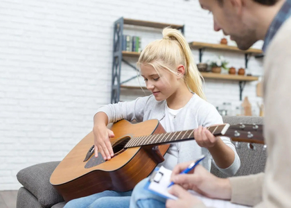 Een meisje speelt gitaar terwijl een volwassene aantekeningen maakt.