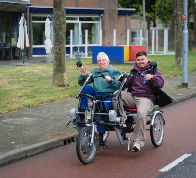 Twee mannen op een tandemfiets lachen en zwaaien.