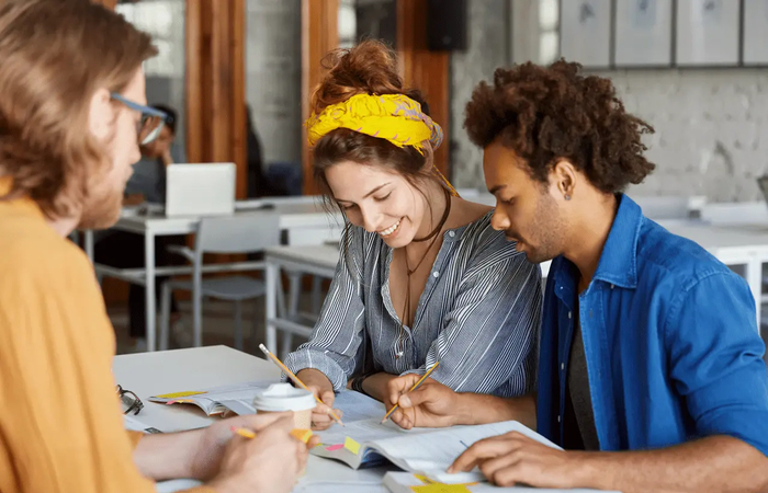 Drie studenten werken samen aan een project met boeken en notities.