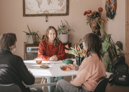 Drie mensen zitten aan tafel met thee en bloemen.