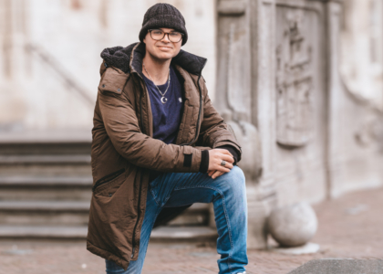 Jonge man in een winterjas poseert op een stenen rand.