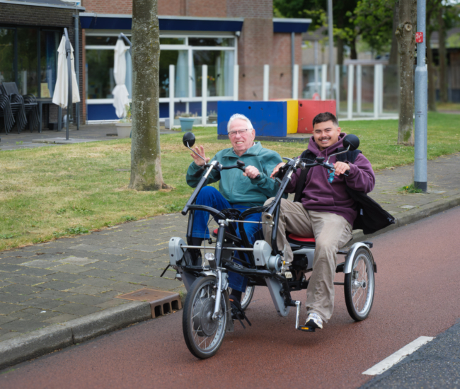 Twee mannen op een tandemfiets lachen en zwaaien.