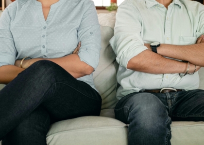 Een man en vrouw zitten met gekruiste armen op een bank.