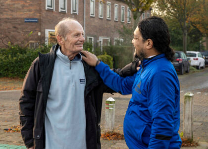 Twee mannen lachen en begroeten elkaar op straat.
