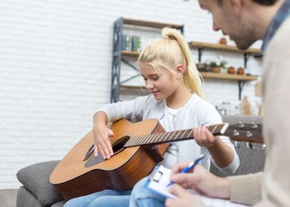 Een meisje speelt gitaar terwijl een volwassene aantekeningen maakt.