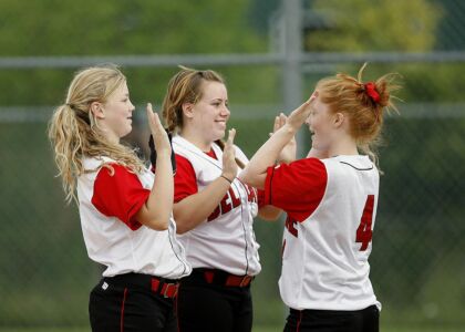 Drie meisjes in sportoutfits vieren samen op het softbalveld.
