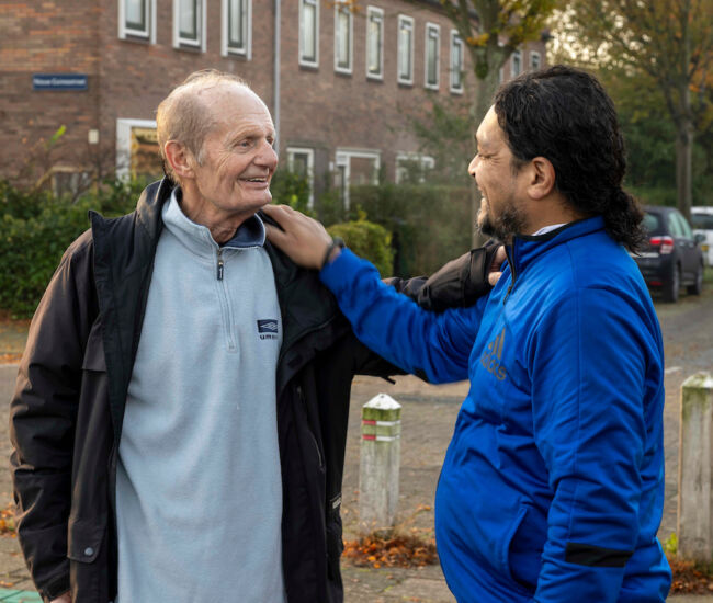 Twee mannen lachen en begroeten elkaar op straat.