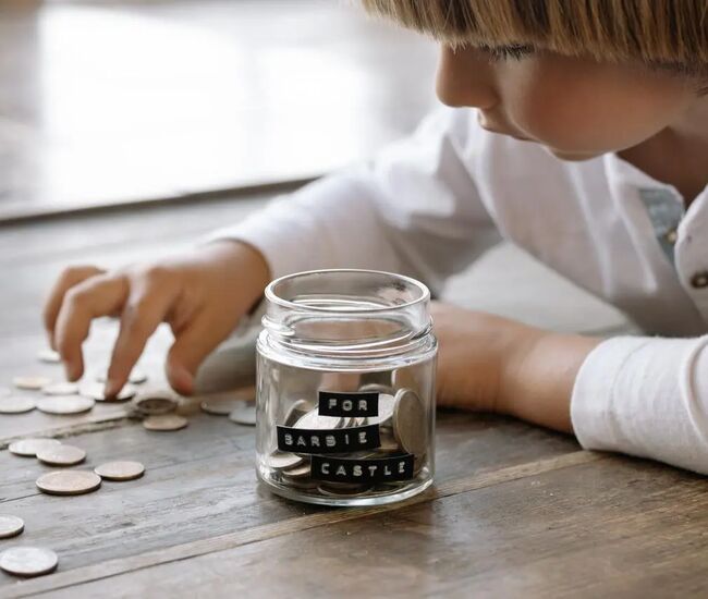 Een kind telt munten voor een spaarpot met "Barbie Castle".