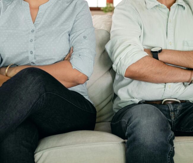 Een man en vrouw zitten met gekruiste armen op een bank.