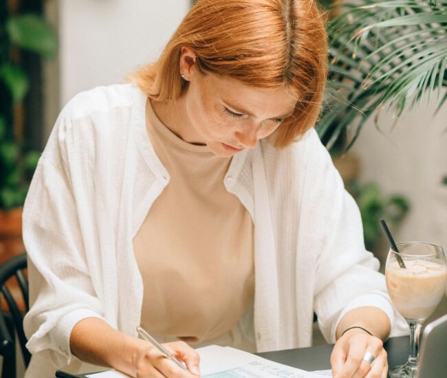 Een vrouw werkt geconcentreerd aan een bureau met documenten en een laptop.