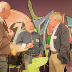 Drie mannen in gesprek met kleurrijke graffiti op de achtergrond.