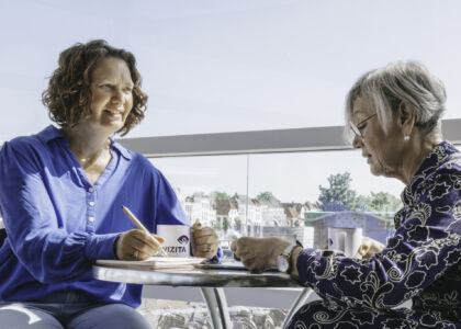 Twee vrouwen in gesprek aan een tafel met uitzicht.