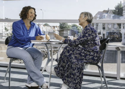Twee vrouwen zitten aan een tafel en hebben een gesprek met koffie.