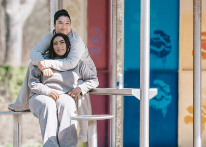 Twee jonge vrouwen zitten samen op een bank onder een overkapping.