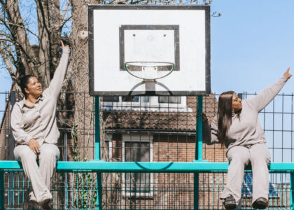 Twee vrouwen zitten op een basketbalring en wijzen omhoog.