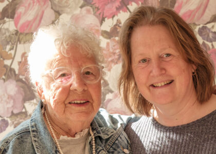 Twee vrouwen poseren samen voor een bloemenachtergrond.