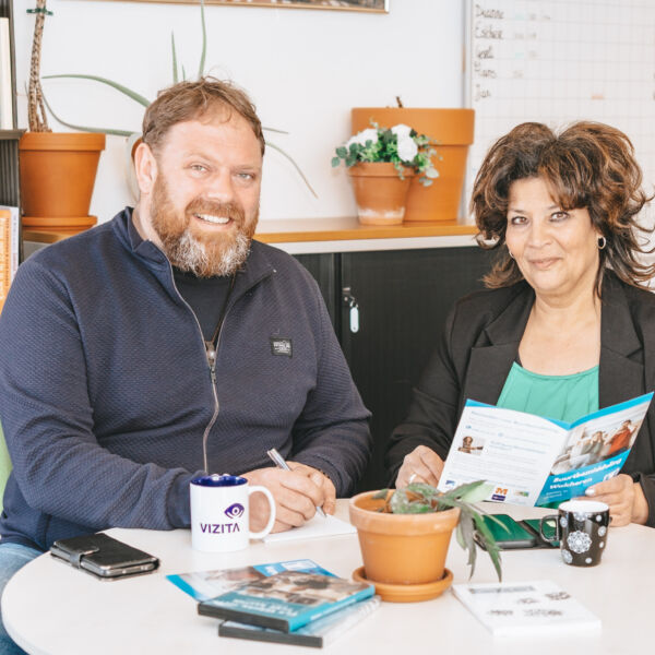 Twee mensen zitten aan een tafel met boeken en een plant.