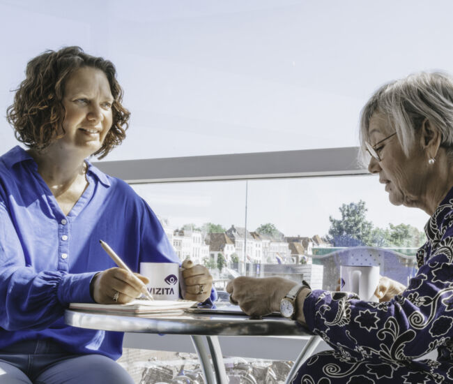 Twee vrouwen in gesprek aan een tafel met uitzicht.