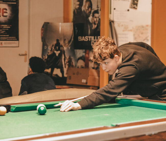 Jongere speelt biljart in een gezellige ruimte met vrienden.