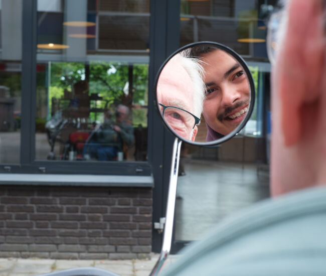 Twee mannen glimlachen naar elkaar in een spiegel.