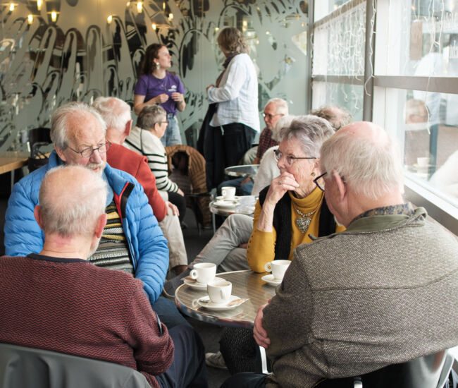 Een groep ouderen zit samen in een café en praat.