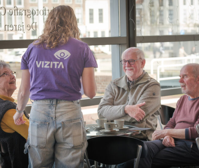 Een jongere praat met ouderen in een café.