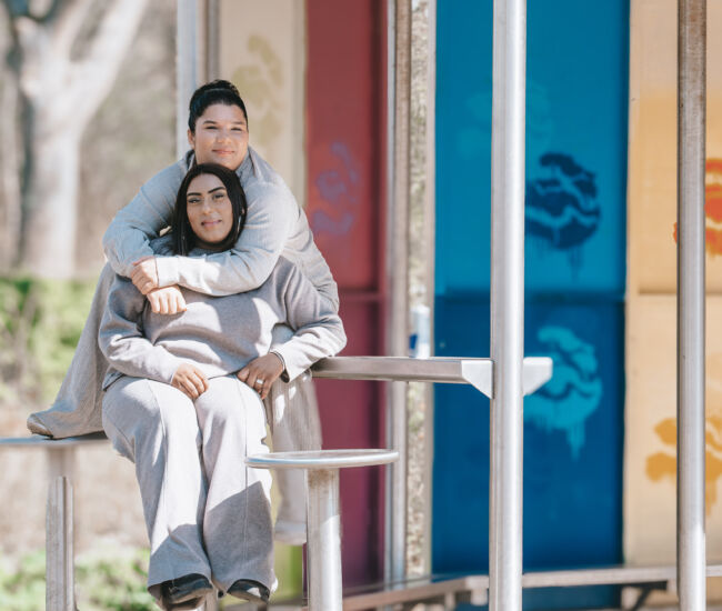 Twee jonge vrouwen zitten samen op een bank onder een overkapping.