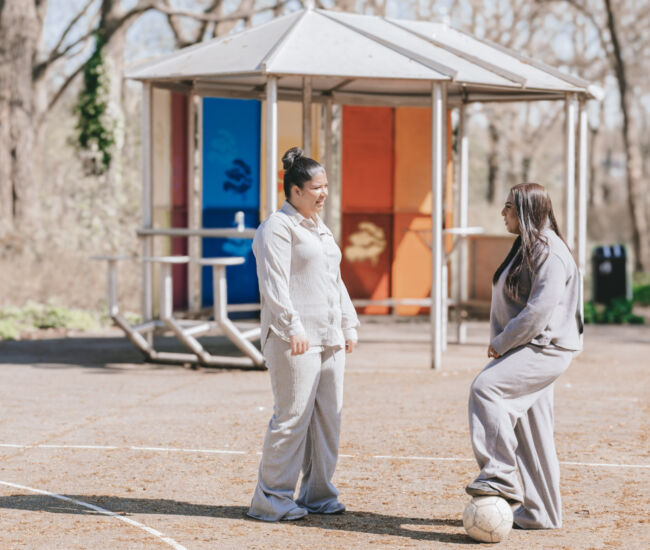 Twee vrouwen in sportkleding praten op een voetbalveld.
