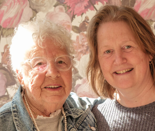 Twee vrouwen poseren samen voor een bloemenachtergrond.