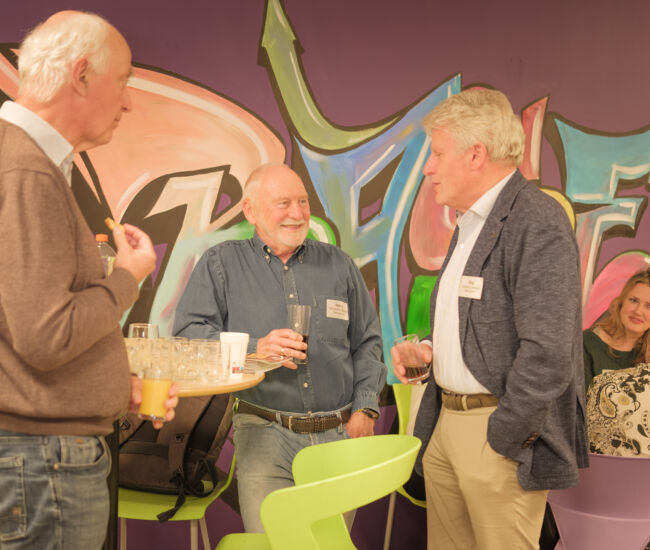 Drie mannen in gesprek met kleurrijke graffiti op de achtergrond.