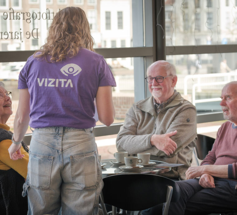Een jongere praat met ouderen in een café.
