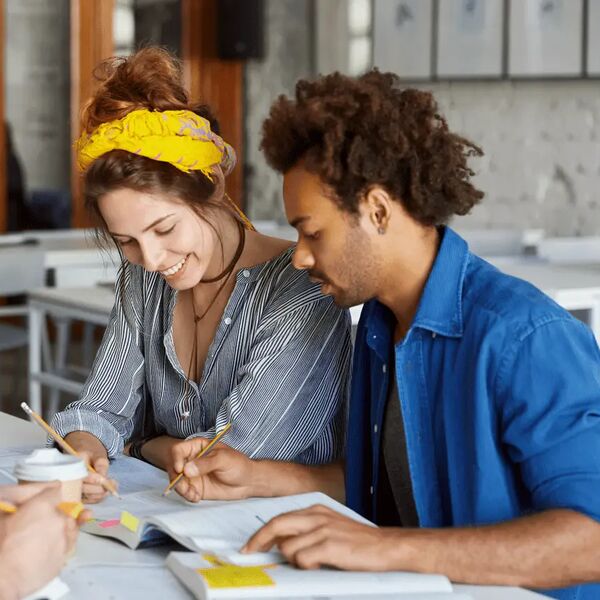 Drie studenten werken samen aan een project met boeken en notities.