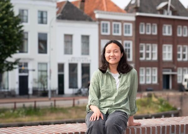 Jonge vrouw met bruin haar zit op een muur, stadsachtergrond.