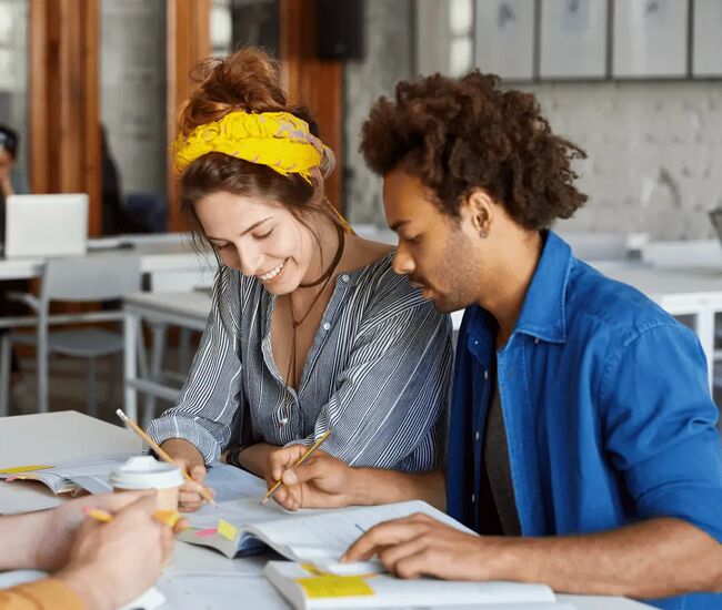 Drie studenten werken samen aan een project met boeken en notities.