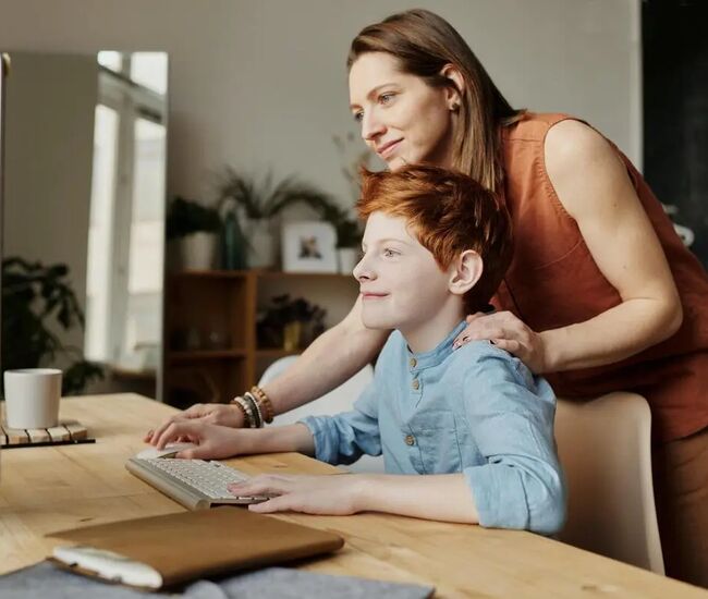 Een moeder helpt haar kind achter de computer.