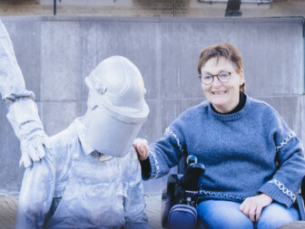 Vrouw in rolstoel poseert naast een beeld van een mijnwerker.