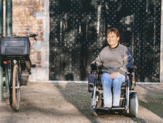 Vrouw in rolstoel poseert naast een fiets in een straat.