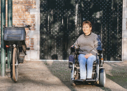 Vrouw in rolstoel poseert naast een fiets in een straat.