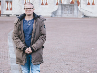 Jongeman in een park met historische gebouwen op de achtergrond.