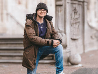 Jonge man in een winterjas poseert op een stenen rand.