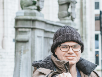 Man met een muts en jas, wijst met zijn hand naar de camera.