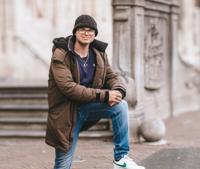 Jonge man in een winterjas poseert op een stenen rand.