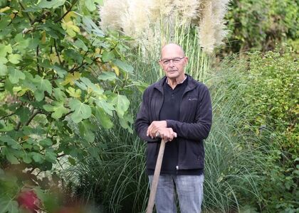 Een man met een stok staat tussen groene planten.