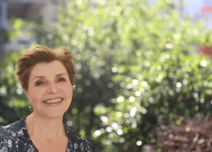 Vrouw met een glimlach, staand voor een groene achtergrond.