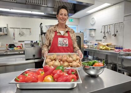 Vrouw in een keuken met groenten en een schort, glimlachend.