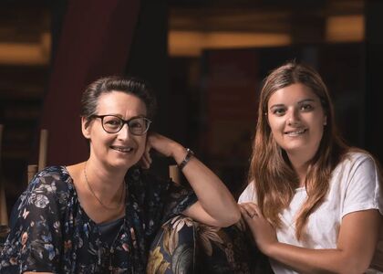 Twee vrouwen zitten samen en lachen naar de camera.