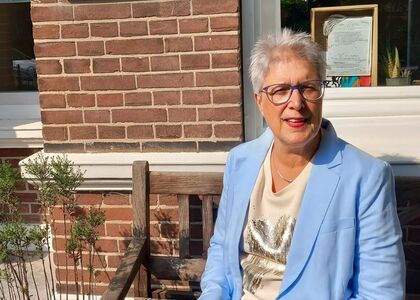 Vrouw in een lichtblauwe blazer zit op een houten bank.