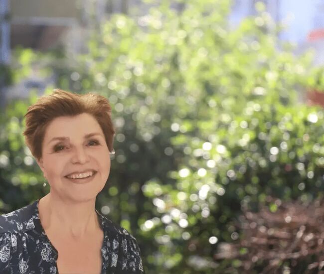 Vrouw met een glimlach, staand voor een groene achtergrond.